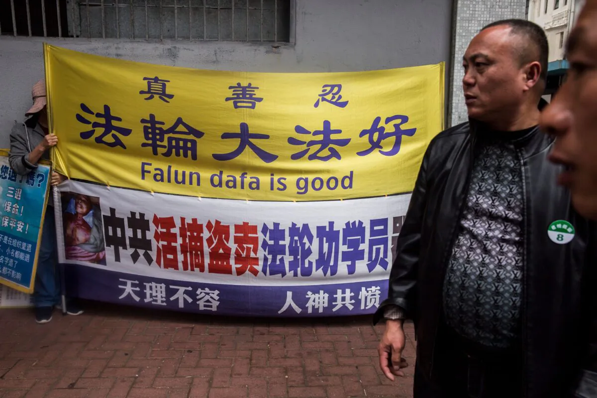 A Falun Gong practitioner (L) holds a sign next to men (R) from a mainland Chinese tour group in the Kowloon district of Hong Kong on Jan. 6, 2019. (Isaac Lawrence/AFP via Getty Images)