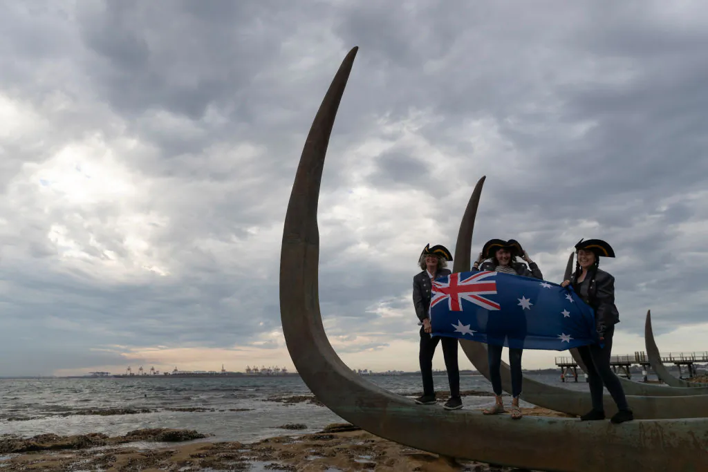 Three women wave the Australian flag at a new installation at the site Lieutenant James Cook is believed to have first stepped ashore on April 29, 2020 in Sydney, Australia. (Brook Mitchell/Getty Images)