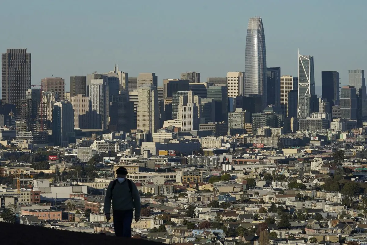 A person wears a protective mask as he walks in front of the skyline on Bernal Heights Hill during the coronavirus pandemic in San Francisco, Calif., on Dec. 7, 2020. (Jeff Chiu/AP Photo)
