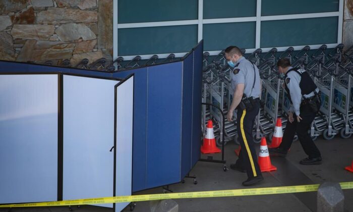 RCMP officers search around rows of luggage carts as screens block off an area of the sidewalk after a shooting outside the international departures terminal at Vancouver International Airport, in Richmond, B.C., on May 9, 2021. (Darryl Dyck / The Canadian Press)