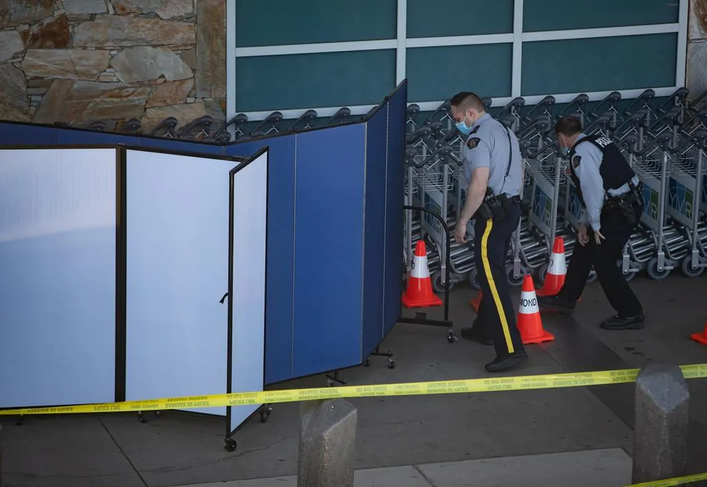 RCMP officers search around rows of luggage carts as screens block off an area of the sidewalk after a shooting outside the international departures terminal at Vancouver International Airport, in Richmond, B.C., on May 9, 2021. (Darryl Dyck / The Canadian Press)