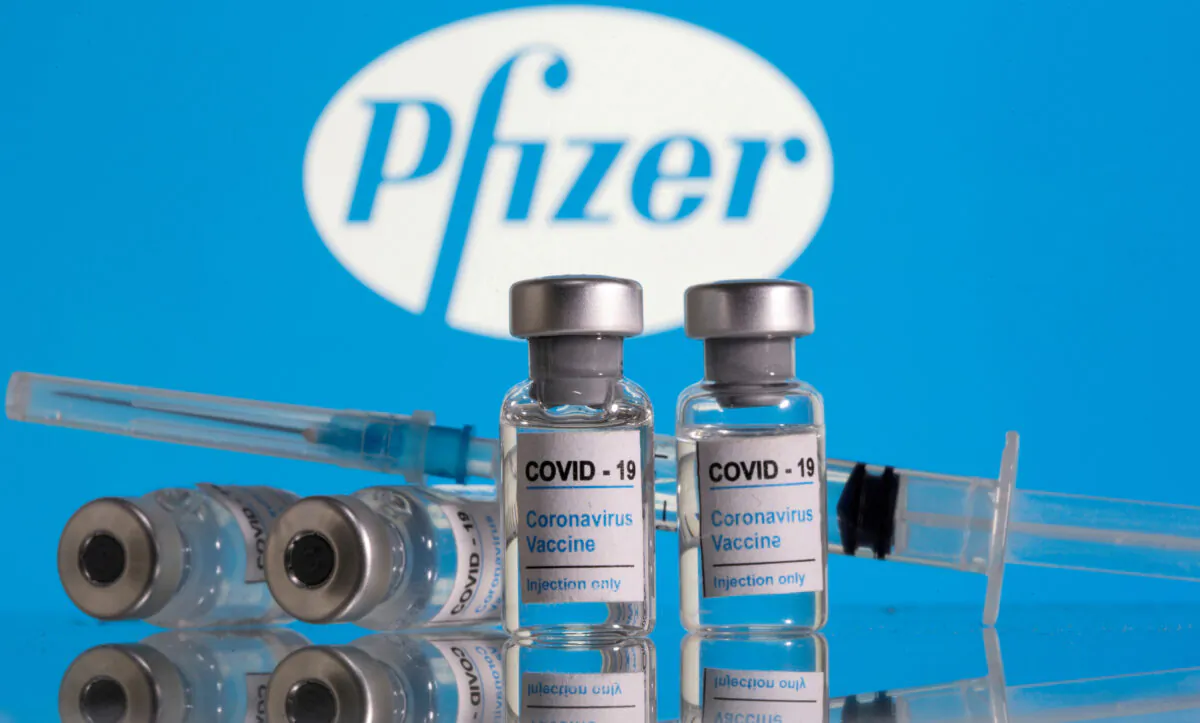 Vials labelled "COVID-19 Coronavirus Vaccine" and a syringe are seen in front of the Pfizer logo in this illustration taken on Feb. 9, 2021. (Dado Ruvic/Reuters)