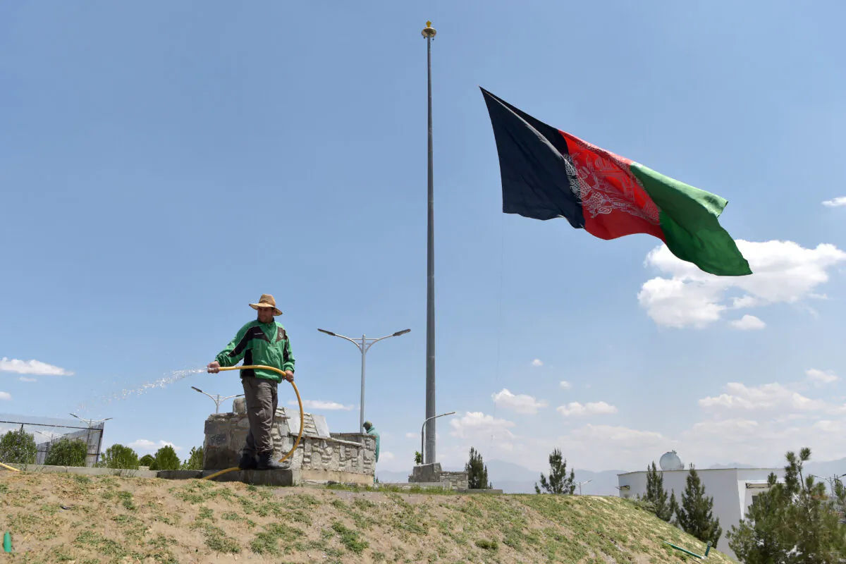 A worker waters a lawn near an Afghan national flag flying at half-mast in Kabul on May 11, 2021. May 11 was declared a national day of mourning by Afghan President Ashraf Ghani to condemn the recent terrorist attacks. (WAKIL KOHSAR/AFP via Getty Images)