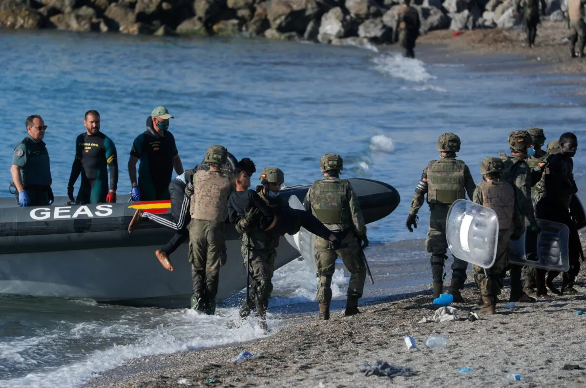 Spanish soldiers help Moroccan citizens at El Tarajal beach, near the fence between the Spanish-Moroccan border, after thousands of migrants swam across the border, in Ceuta, Spain, on May 19, 2021. (Jon Nazca/Reuters)