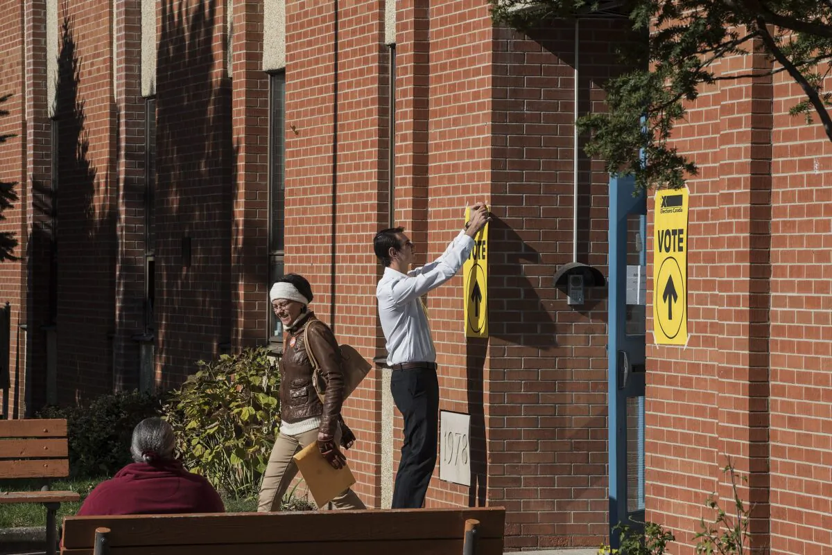 An Elections Canada volunteer tapes up signs at a polling station in Toronto on Oct. 19, 2015. (The Canadian Press/Aaron Vincent Elkaim)