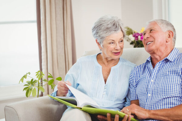 Senior,Couple,Sitting,On,Sofa,And,Reading,A,Book,In