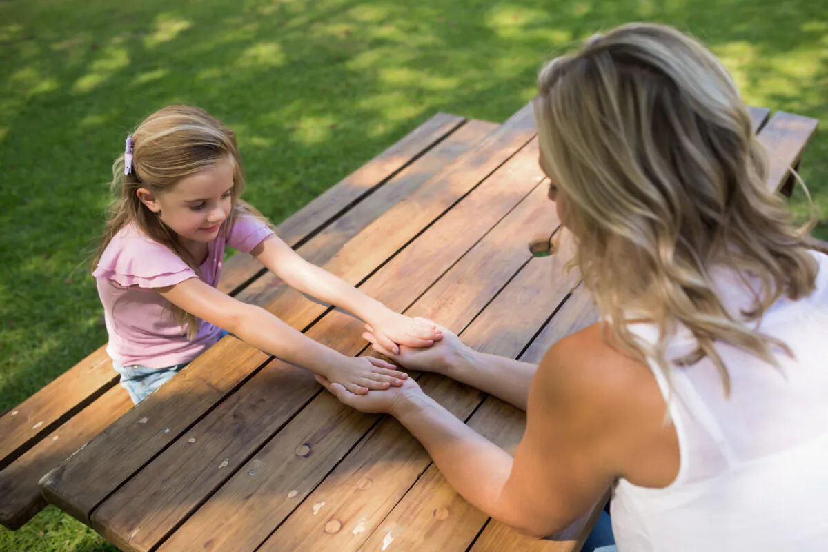 Mother and daughter holding hands on picnic table in park (Shutterstock)