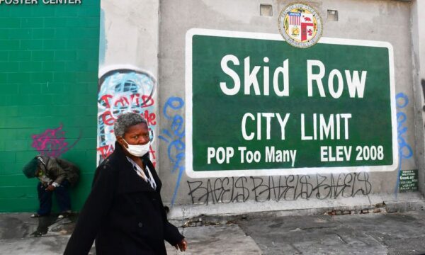 A woman walks past a Skid Row sign pointing out a population of “Too Many” in Los Angeles, on April 26, 2021. (Frederic J. Brown/AFP via Getty Images)