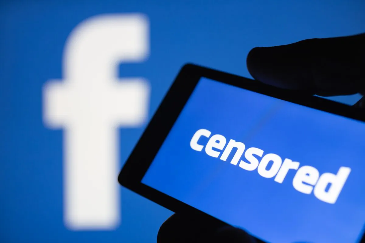 A smartphone in hand displaying the word "censored" in front of a blurred Facebook logo. (klevo/Shutterstock)