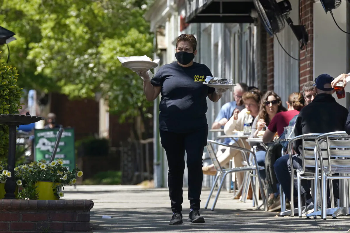 A member of the wait staff delivers food to outdoor diners along the sidewalk at the Mediterranean Deli restaurant in Chapel Hill, N.C., on April 16, 2021. (Gerry Broome/AP Photo)