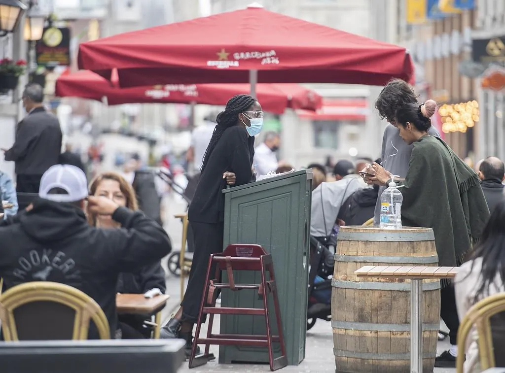A greeter wears a face mask as people wait for a table at a restaurant in Old Montreal, on May 30, 2021, as the COVID-19 pandemic continues in Canada and around the world. (The Canadian Press/Graham Hughes