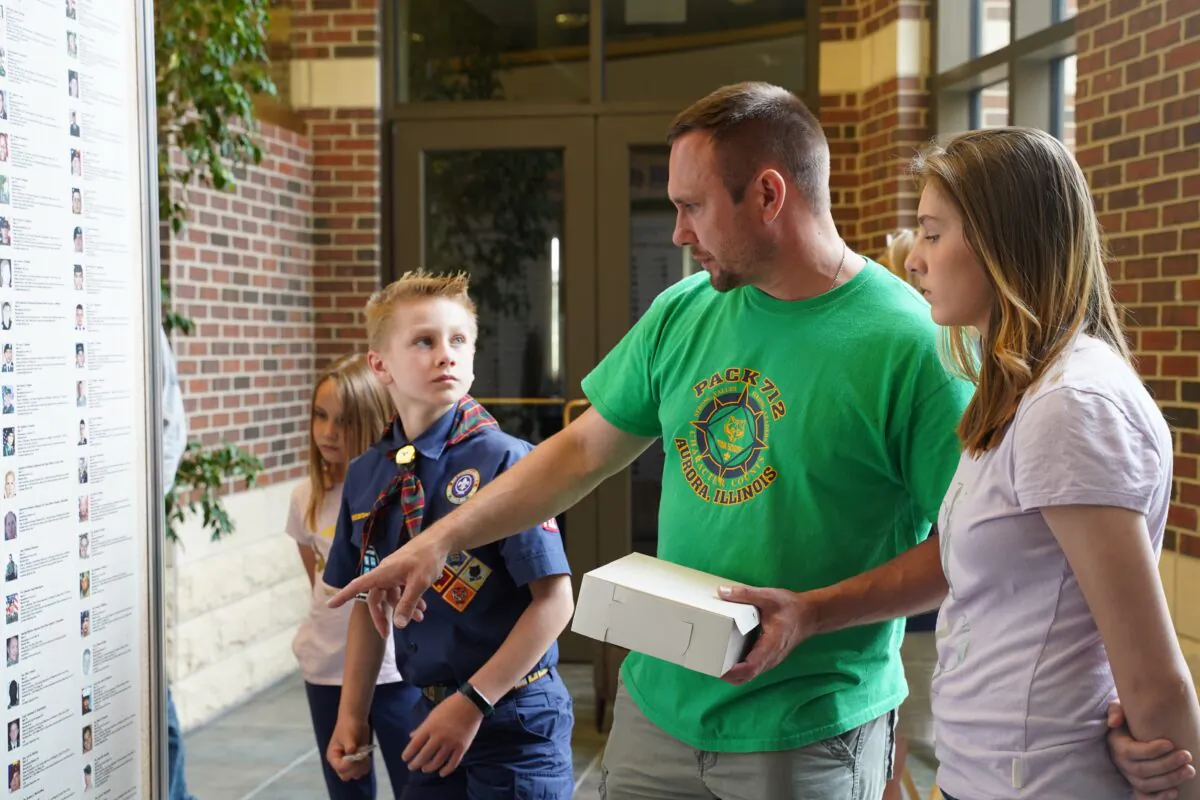 Drew Barczak tells his children about the fallen soldiers on a Wall of Honor displayed at Oswego Township Hall in Oswego, Illinois on May 31, 2021. (Cara Ding/The Epoch Times)