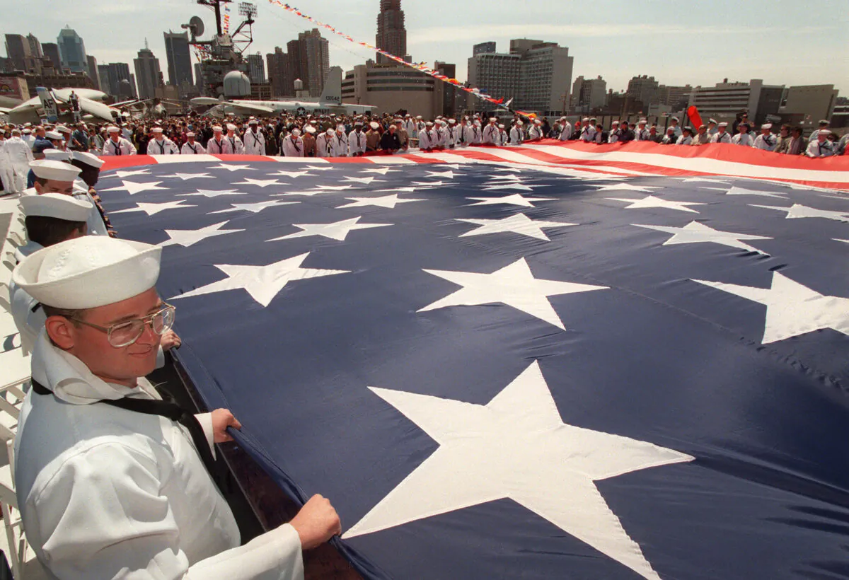 A U.S. war veterans and active duty personnel join others in rolling up a fifty by ninety-foot U.S. flag on the deck of the Intrepid Sea Air Space Museum in New York, during a Memorial Day ceremony, on May 26, 1997. (Stan Honda/AFP via Getty Images)