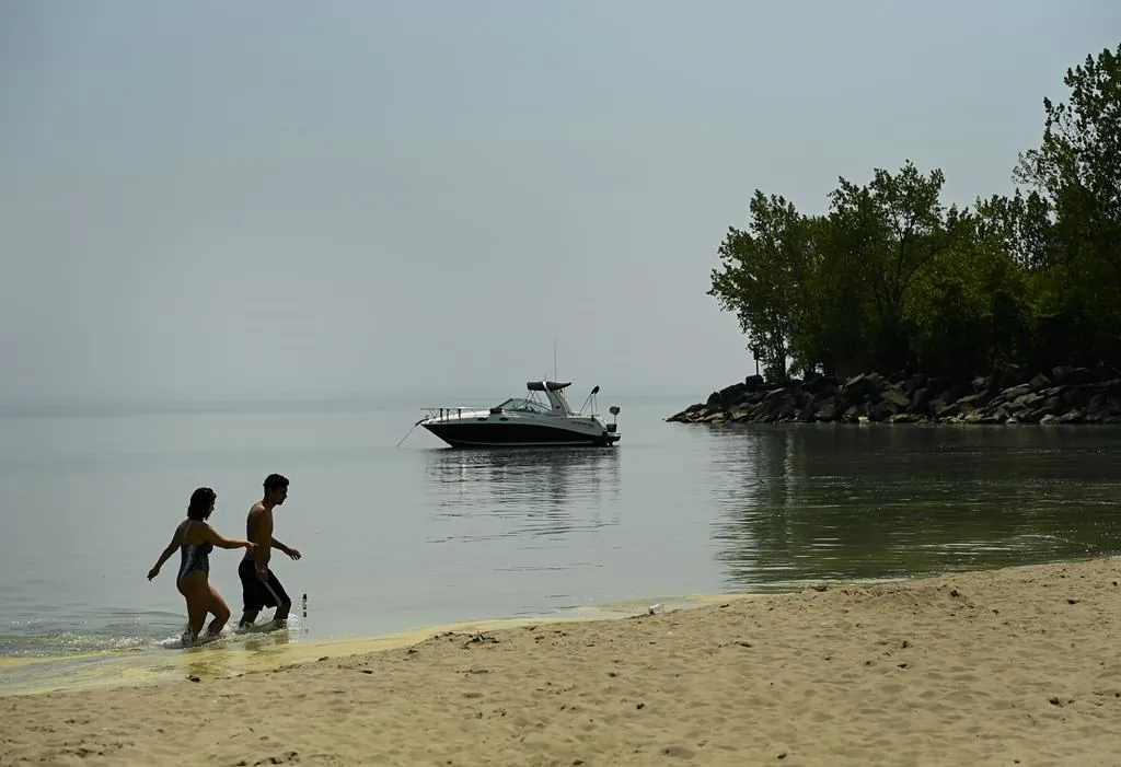 People walk in Lake Ontario on a warm sunny day at Woodbine Beach during the COVID-19 pandemic in Toronto on May 25, 2021. (The Canadian Press/Nathan Denette)