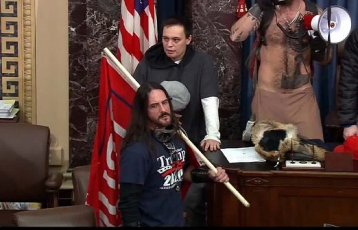 In this image from closed circuit television footage, a man identified as Paul Hodgkins, front, holds a flag while in the Senate chamber inside the U.S. Capitol in Washington on Jan. 6, 2021. (CCTV via FBI)