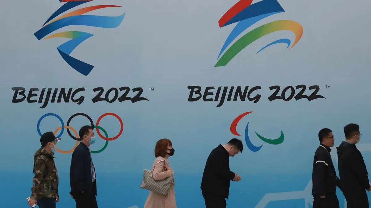 People wear protective masks as they walk in front the logos of the 2022 Beijing Winter Olympics at National Aquatics Centre in Beijing, China, on April 9, 2021. (Lintao Zhang/Getty Images)