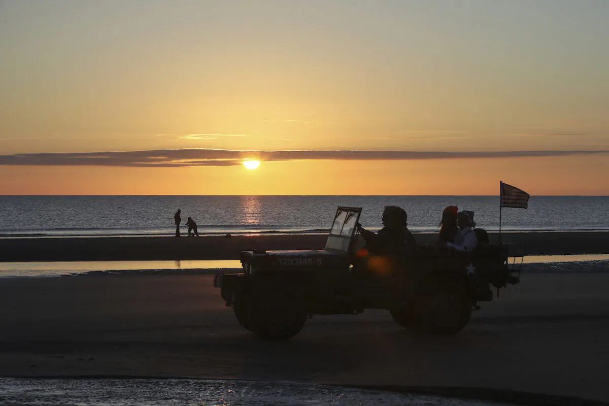 World War II reenactors drive a jeep at dawn on Omaha Beach in Saint-Laurent-sur-Mer, Normandy, France, on June 6, 2021. (David Vincent/AP Photo)