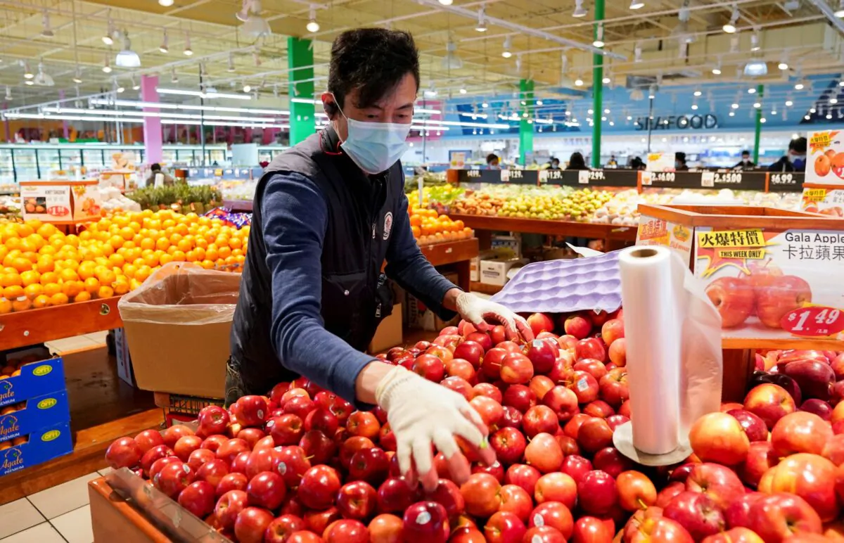 Wearing a mask and gloves, a worker re-stocks apples in an Asian grocery store in Falls Church, Va., on April 3, 2020. (Kevin Lamarque/Reuters)