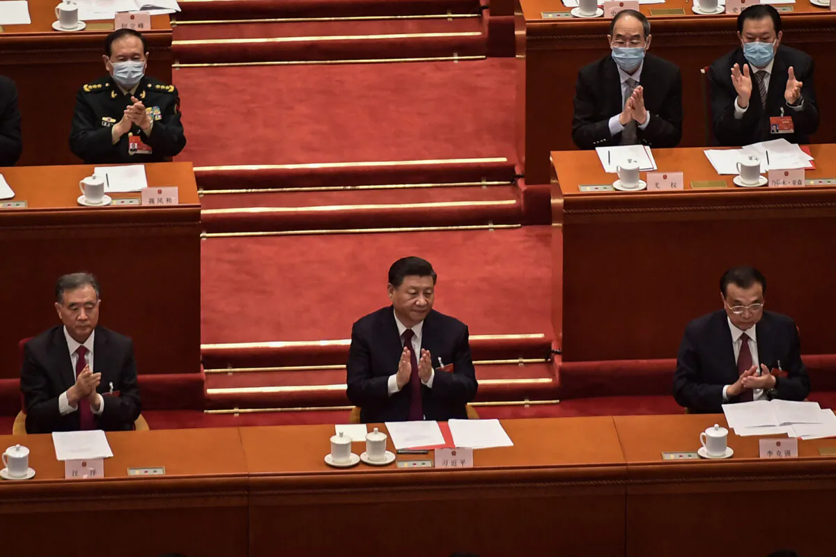Politburo Standing Committee member Wang Yang (left), Chinese leader Xi Jinping (center), and Premier Li Keqiang applaud after the result of the vote on changes to Hong Kong's election system was announced during the closing session of the National Peoples Congress (NPC) at the Great Hall of the People in Beijing on March 11, 2021. (Nicolas Asfouri/AFP via Getty Images)