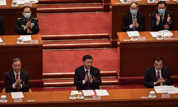 Politburo Standing Committee member Wang Yang (L), President Xi Jinping (C) and Premier Li Keqiang applaud after the result of the vote on changes to Hong Kong's election system was announced during the closing session of the National Peoples Congress (NPC) at the Great Hall of the People in Beijing on March 11, 2021. (Nicolas Asfouri/AFP via Getty Images)