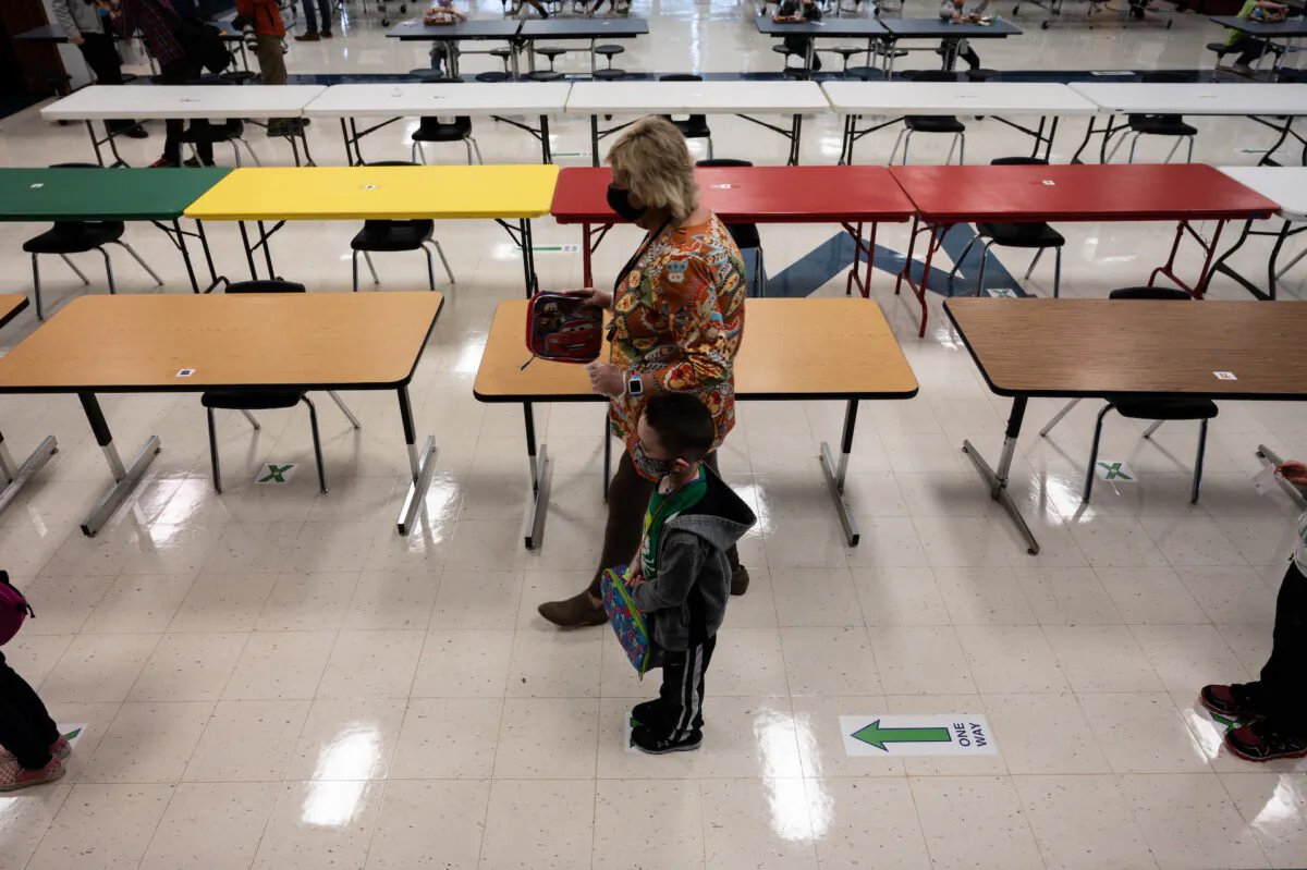 A masked teacher walks by as students wait in a single file line after eating a socially distanced lunch at Medora Elementary School in Louisville, Ky., on March 17, 2021. (Jon Cherry/Getty Images)