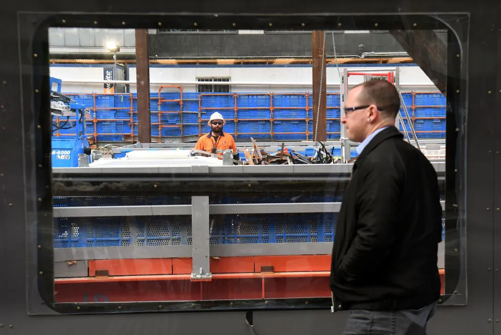 A passer-by looks through a window at a man working on a construction site in Melbourne, Australia on July 2, 2019. (William West/AFP via Getty Images)