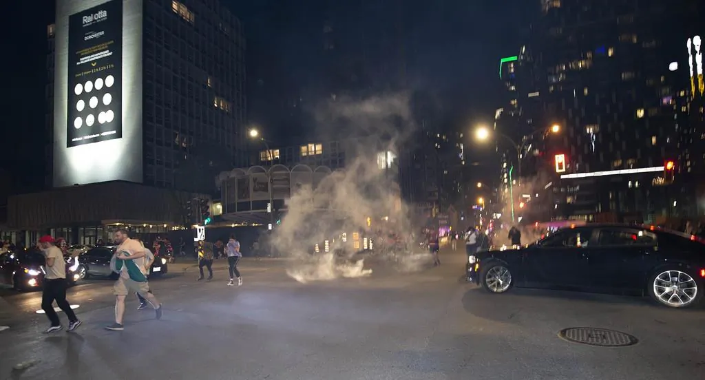 Montreal Canadiens fans run from tear gas fired by the police to break up the huge crowds as Canadiens fans celebrate on Rue Rene Levesque after the Canadiens defeated the Vegas Golden Knights in overtime game 6 NHL Stanley Cup playoff hockey semifinal action in Montreal, on June 24, 2021. (The Canadian Press/Peter McCabe)