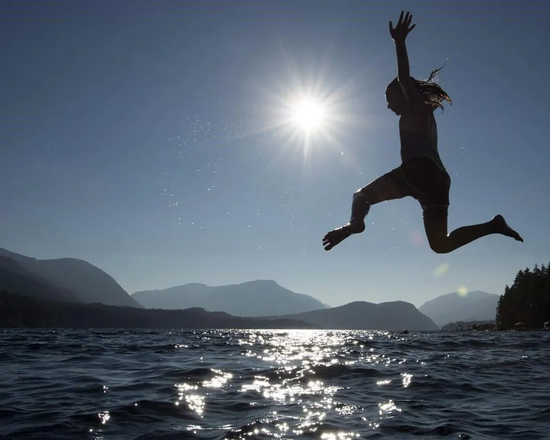 A young girl is silhouetted against the sun as she jumps in the waters of Sproat Lake in Port Alberni, B.C. on August, 31, 2018. (The Canadian Press/Jonathan Hayward)