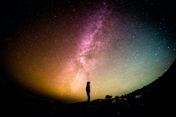 A person stands and looks up at the Milky Way at night