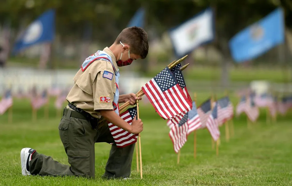 A Boy Scout places miniature American flags at graves ahead of Memorial Day in the Los Angeles National Cemetery on May 29, 2021. (AGUSTIN PAULLIER/AFP via Getty Images)
