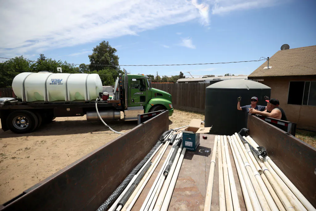 Chris McMillan with AEI Transportation, talks with Loren Scott Denney as she fills a tanks with potable water during the installation of a 2,500 gallon tank in front of his house after his well went dry on May 25, 2021, in Madera, California. Loren Scott Denney received a 2,500 gallon water tank from Central Valley nonprofit community development organization Self Help Enterprises after his well went dry. (Justin Sullivan/Getty Images)