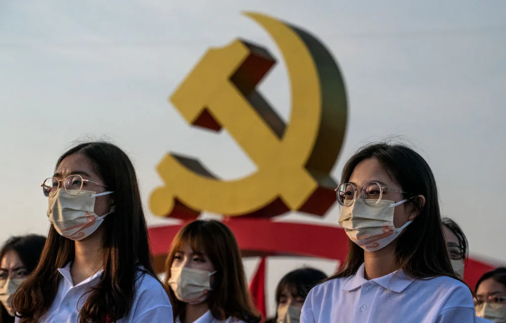 Chinese women stand in front of a large Communist Party logo at a ceremony marking the 100th anniversary of the Communist Party at Tiananmen Square in Beijing, China, on July 1, 2021. (Kevin Frayer/Getty Images)