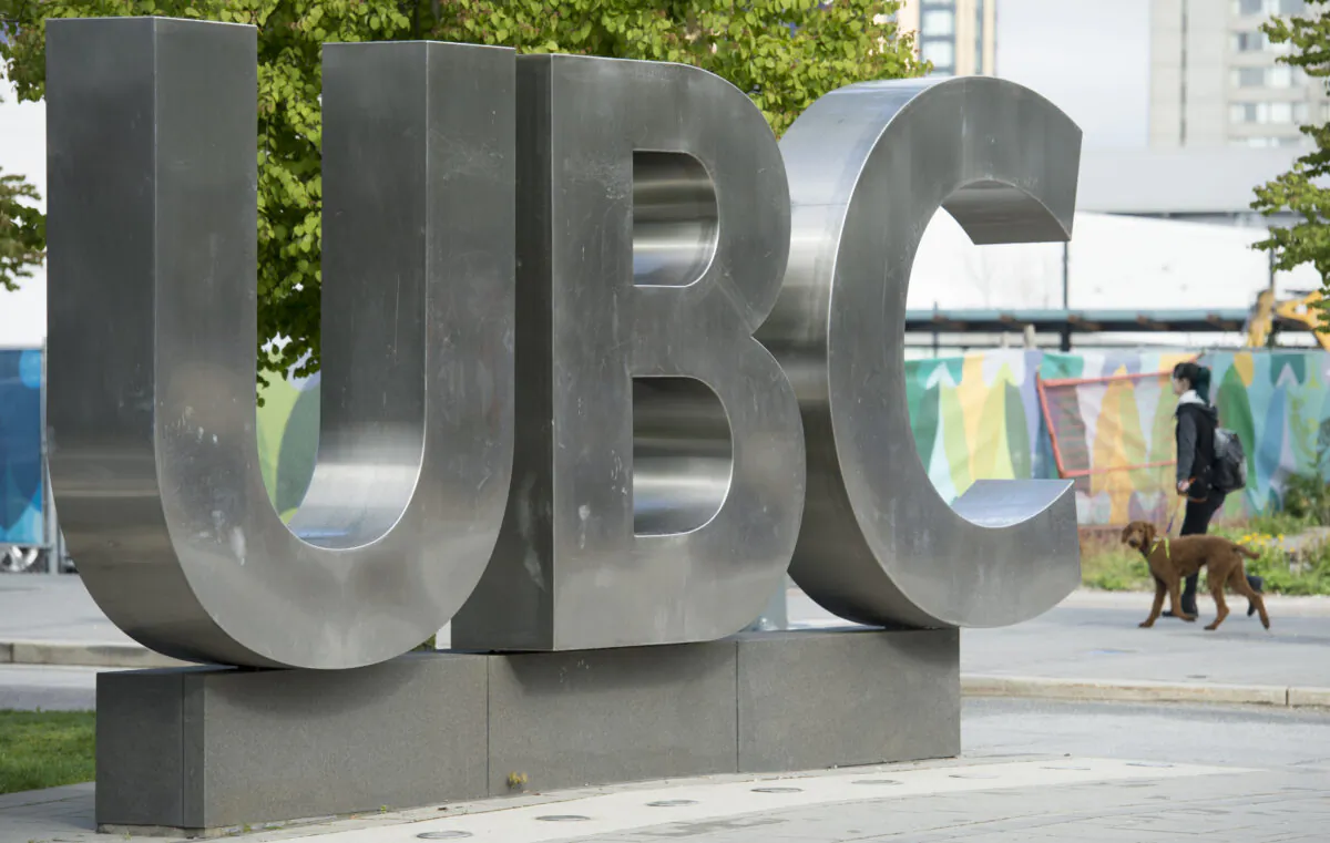 A woman and her dog walk past the UBC sign at the University of British Columbia in Vancouver on Apr. 23, 2019. (The Canadian Press/Jonathan Hayward)