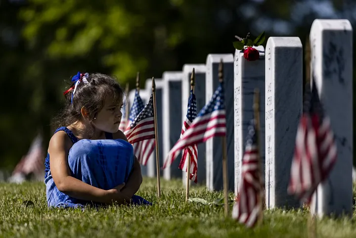 A girl sits in the grass among the headstones of those killed during the 
wars in Iraq and Afghanistan in Section 60 of Arlington National 
Cemetery in Arlington, Va., during Memorial Day on May 31, 2021. 
(Samuel Corum/Getty Images)