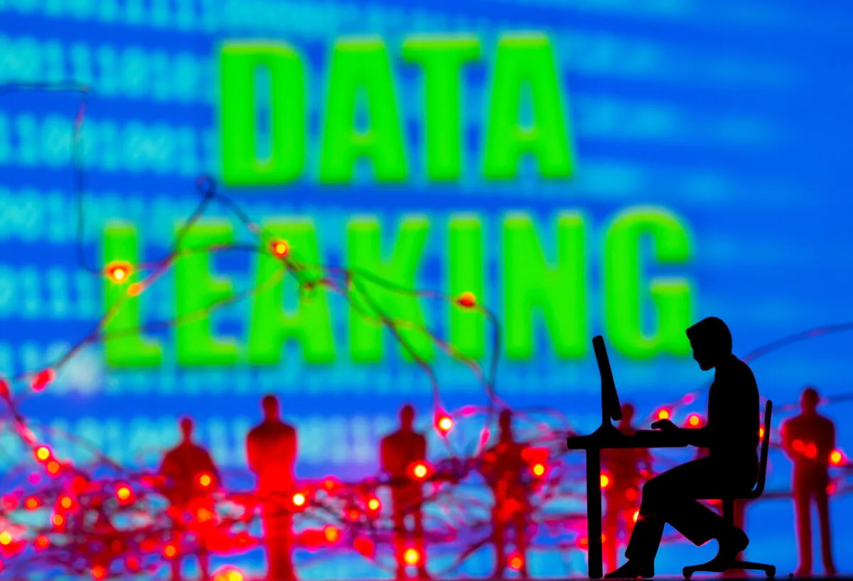 A 3D printed model of a man working on a computer, LED lights and toy people figures are seen in front of displayed binary code and words "Data leaking" in this illustration taken, on July 5, 2021. (Dado Ruvic/Illustration/Reuters)