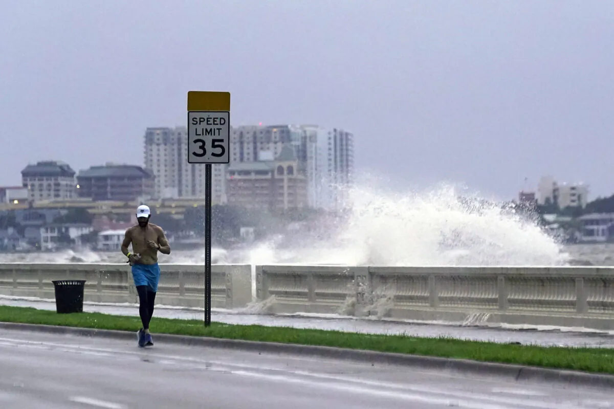 A jogger makes his way along Bayshore Blvd., in Tampa, Fla., as a wave breaks over a seawall, during the aftermath of Tropical Storm Elsa on July 7, 2021. (John Raoux/AP Photo)