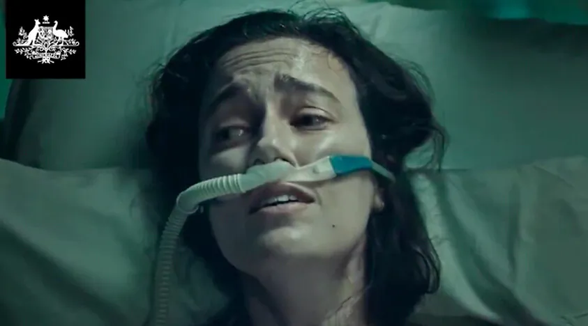 The federal government's new Covid ad depicts a young women struggling to breathe on a hospital bed (Screenshot).