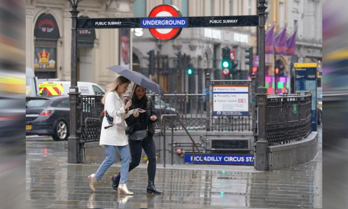 Friends share hand gel as they walk past the entrance to Piccadilly Underground station, London, on June 18, 2021. (Jonathan Brady/PA)