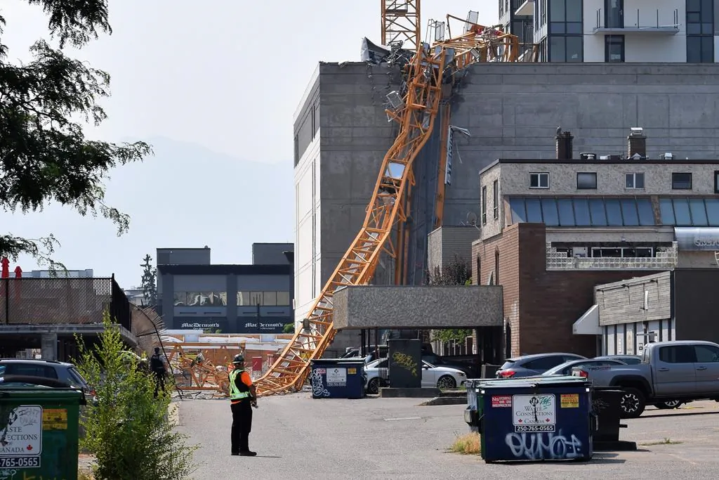 A worker looks on as a police officer investigates a collapsed crane resting on the building it damaged in Kelowna, B.C., Canada, on July 12, 2021. (The Canadian Press/Alistair Waters)