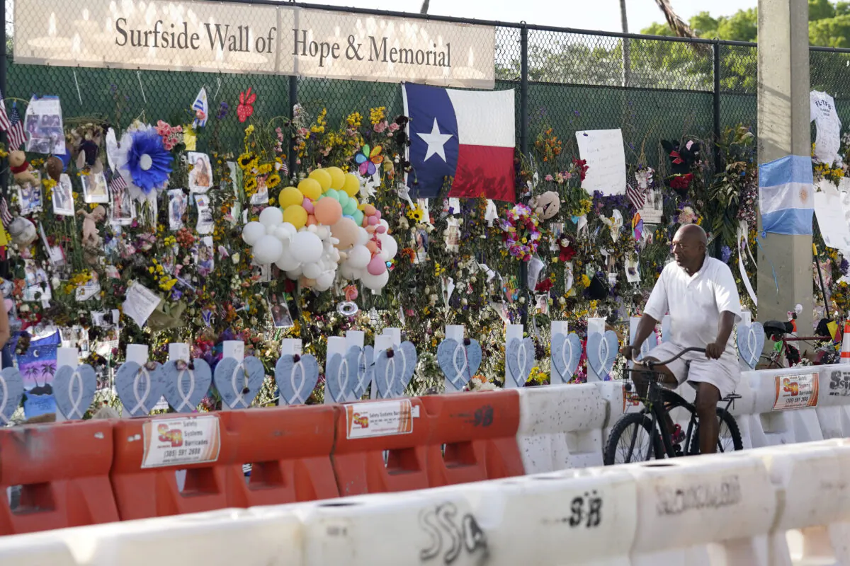A cyclist rides past a makeshift memorial recognizing the victims of the partially collapsed Champlain Towers South building, as removal and recovery work continues at the site, in Surfside, Fla., on July 13, 2021. (Lynne Sladky/AP Photo)