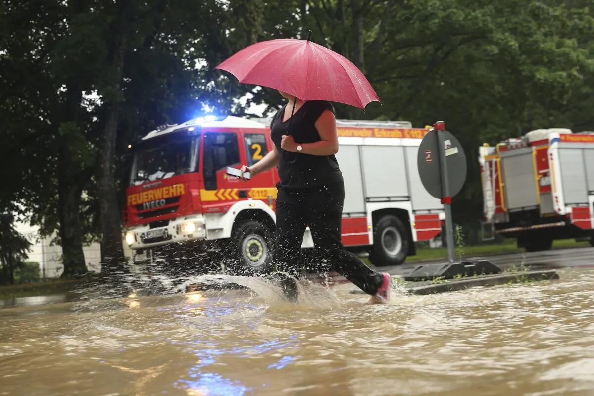 A woman walks past fire trucks at a flooded street with an umbrella Duesseldorf, Germany, on July 14, 2021. (David Young/dpa via AP)
