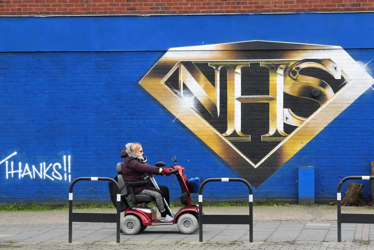 A woman on a mobility scooter drives past a mural praising the NHS, in London on March 5, 2021. (Toby Melville/Reuters)