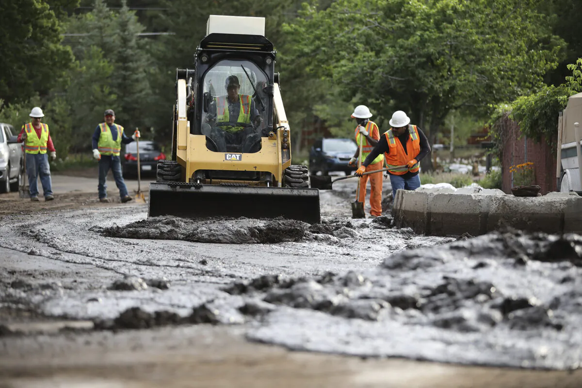 A crew using hand tools and a bobcat work to clear streets after flash flooding in Flagstaff, Ariz., on Wednesday, July 14, 2021. (Jake Bacon/Arizona Daily Sun via AP)