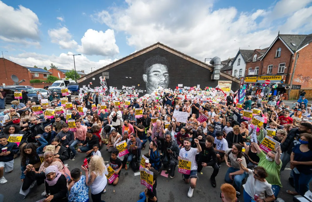 People taking the knee in front of a mural of Manchester United striker and England player Marcus Rashford on Copson Street, Withington, UK, on July 13, 2021. (Danny Lawson/PA)
