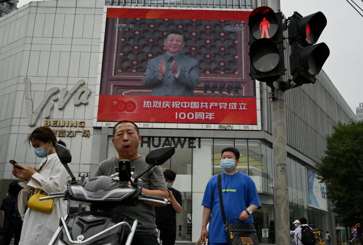 People walk in front of a large screen showing Chinese leader Xi Jinping giving a speech during celebrations to mark the 100th anniversary of the founding of the Chinese Communist Party in Beijing, China on July 1, 2021. (Noel Celis/AFP via Getty Images)