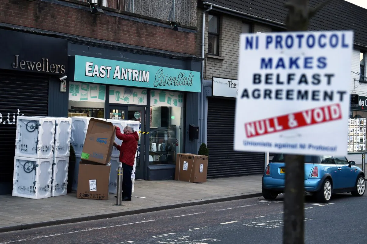 A man sorts through a delivery of washing machines with a sign is seen across the road featuring a message against the Brexit border checks in relation to the Northern Ireland protocol in the town centre of Larne, Northern Ireland, on Feb. 12, 2021. (Clodagh Kilcoyne/Reuters)