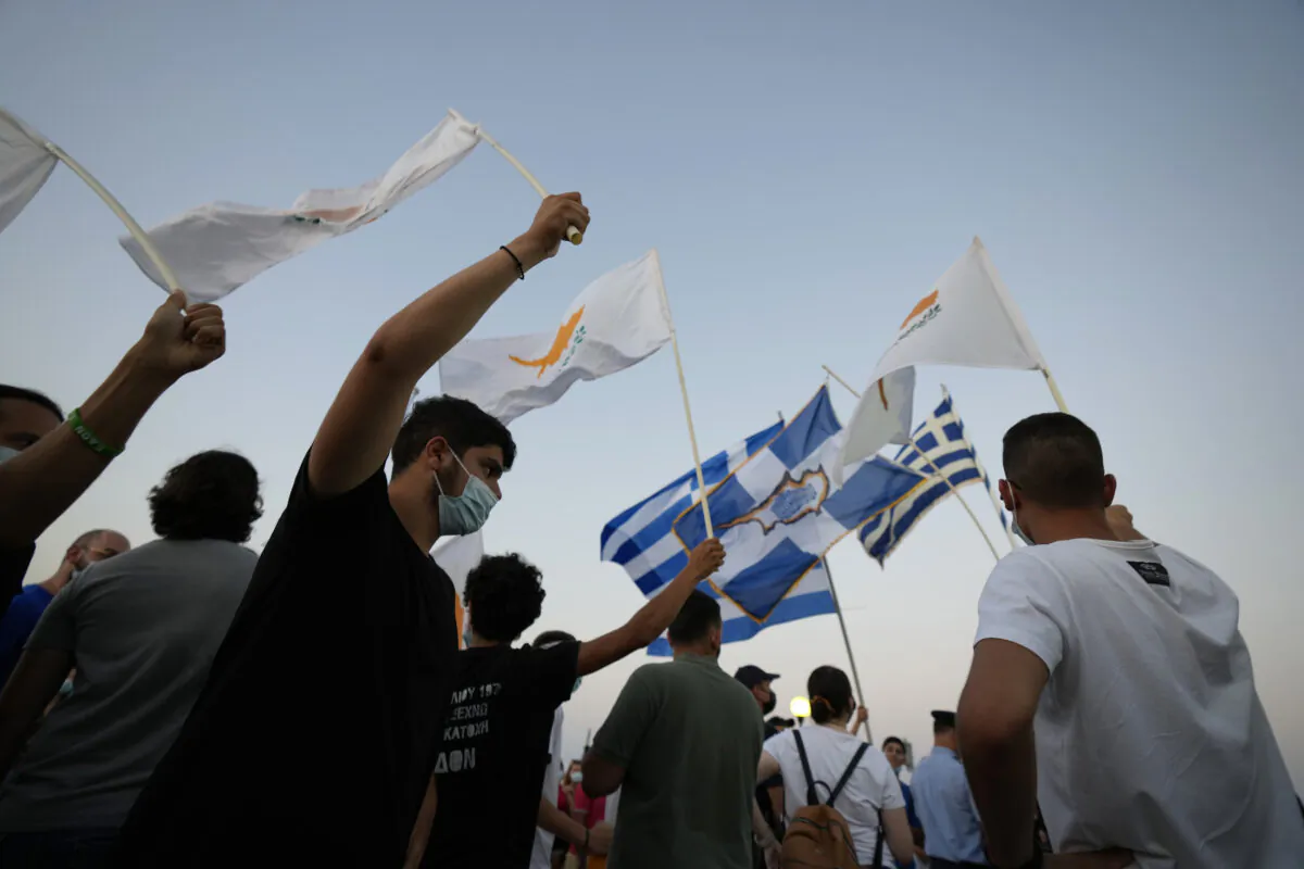 Residents of Varosha or Famagusta, abandoned city, hold Cyprus and Greek flags during a protest against the Turkish President visiting the Turkish occupied part of the island at the north and the 47th anniversary against the Turkish invasion in the island, in Dherynia, Cyprus, on July 19, 2021. (Petros Karadjias/AP Photo)
