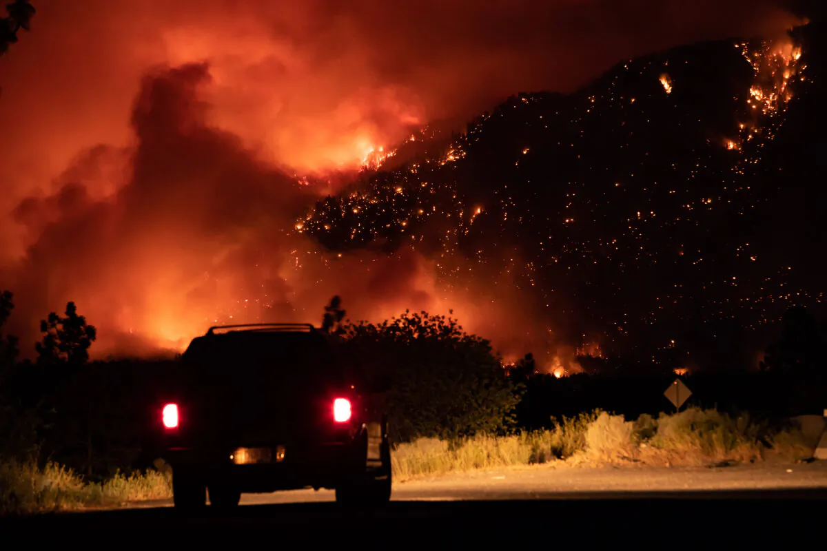 A motorist watches from a pullout on the Trans-Canada Highway as a wildfire burns on the side of a mountain in Lytton, B.C. on July 1, 2021. (The Canadian Press/Darryl Dyck)