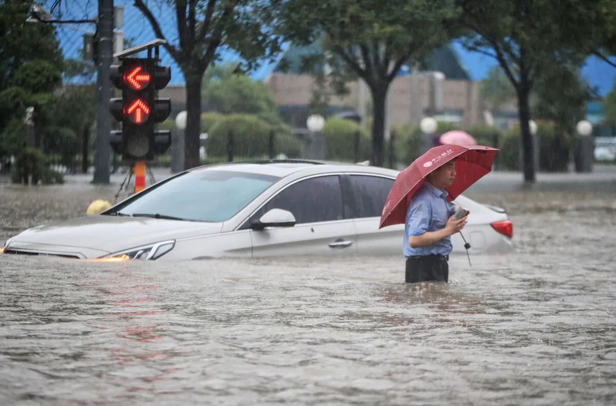 A man is wading past a submerged car along a flooded street following heavy rains in Zhengzhou, Henan Province, China, on July 20, 2021. (STR/AFP via Getty Images)