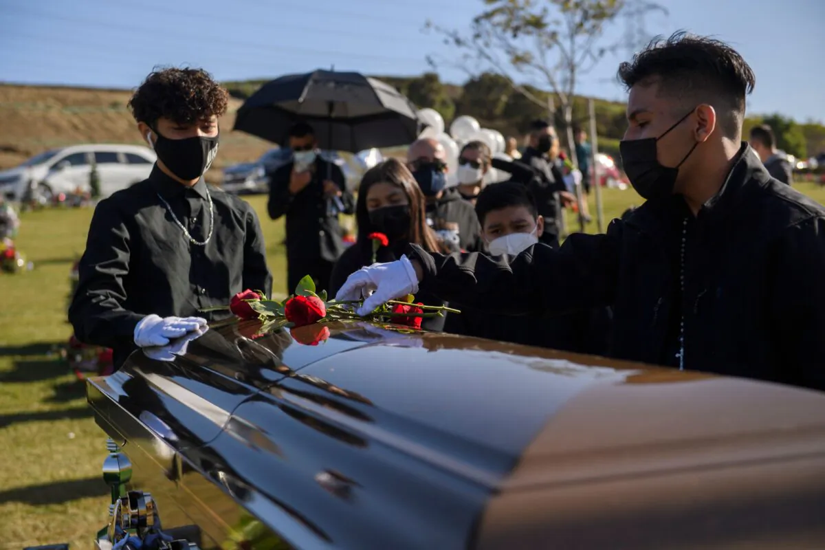 Gilberto Arias, 15, (R) and Javier Dominguez, 13, place flowers on the casket of Gilberto Arreguin Camacho, 58, who died due to COVID-19, during his burial service at a cemetery in Whittier, Calif., on Dec. 31, 2020. (Patrick T. Fallon/AFP via Getty Images)